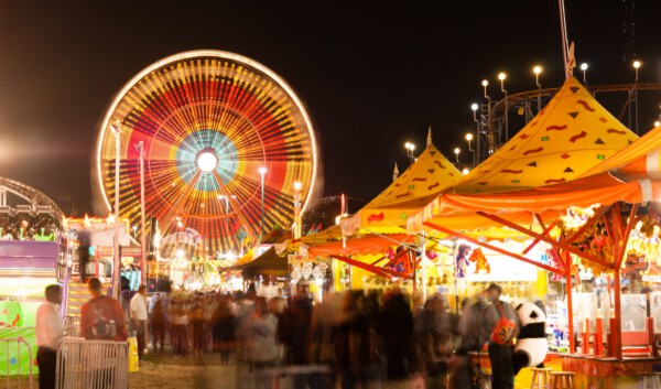 Bright Ferris wheel and carnival booths at night in St. George LA, with crowds walking around.