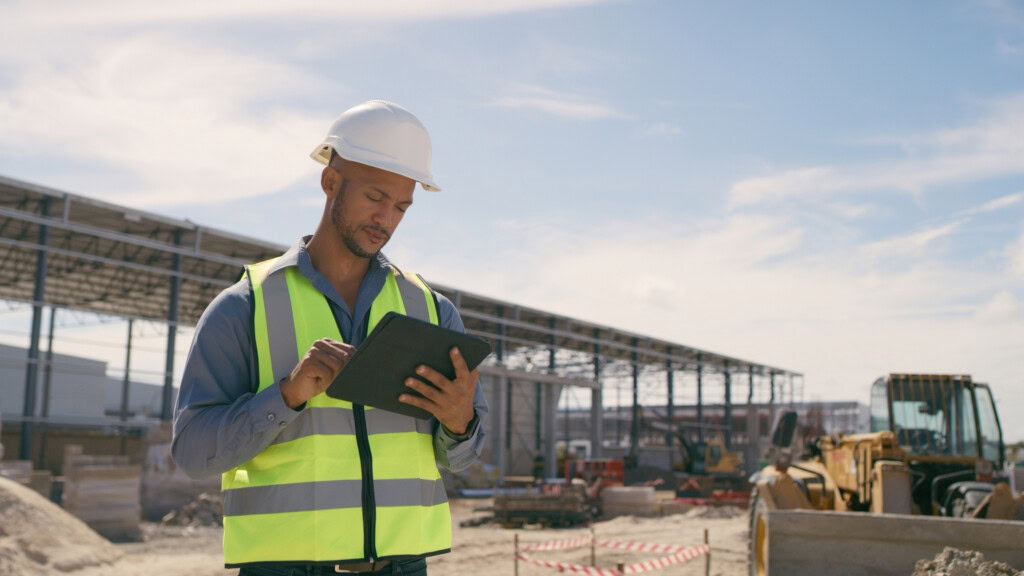Construction worker in vest and helmet uses a tablet at a City of St. George site with equipment nearby.
