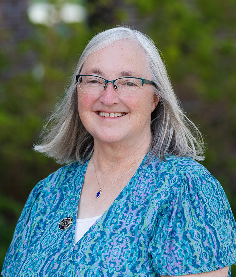 Smiling older woman with gray hair and glasses in a blue patterned shirt outdoors in St. George.